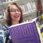 Scarlett B Wile reads a 'fetish' book in a library in glasses. Her luscious tongue licks her lips as she stare seductively at the camera.