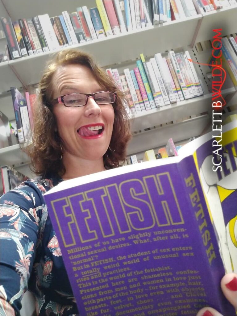 Scarlett B Wile reads a 'fetish' book in a library in glasses. Her luscious tongue licks her lips as she stare seductively at the camera.