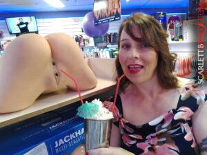 Scarlett B Wilde stands next to a prosthetic vagina with a milkshake covered whipped cream and straws. One for her and one for the vagina. She's standing in Newtown adult shop.