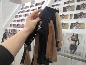 Scarlett B Wilde holds up a collection of pantyhose samples in different colours. She's in the hosiery section of a retail store.