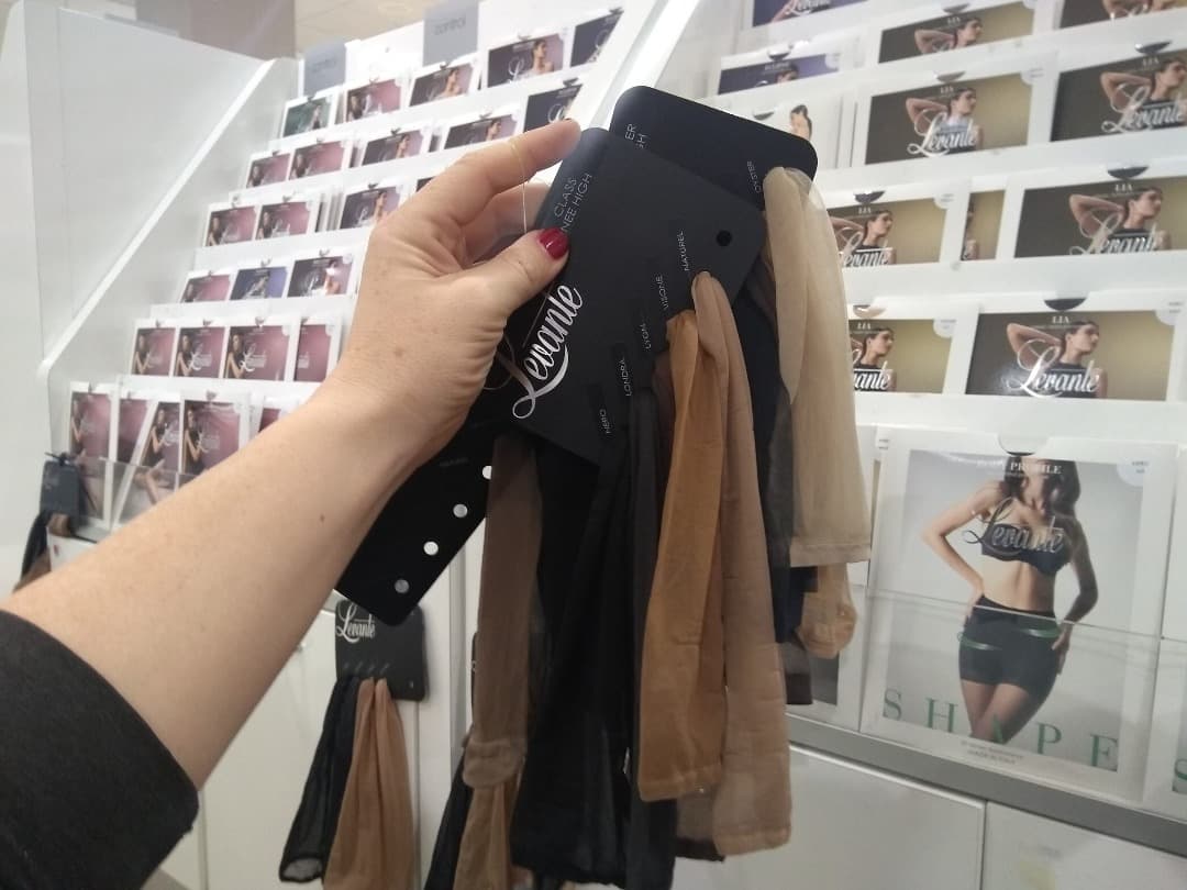 Scarlett B Wilde holds up a collection of pantyhose samples in different colours. She's in the hosiery section of a retail store.