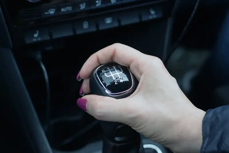 A female hand with purple nail polish handles a manual transmission gear shift